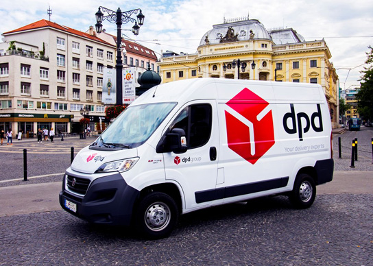 Samochód dostawczy DPD na tle miejskiego placu i budynków.